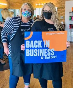 Troy Salon & Day Spa employees holding "Back in Business" sign after reopening from 2020 COVID shutdown.